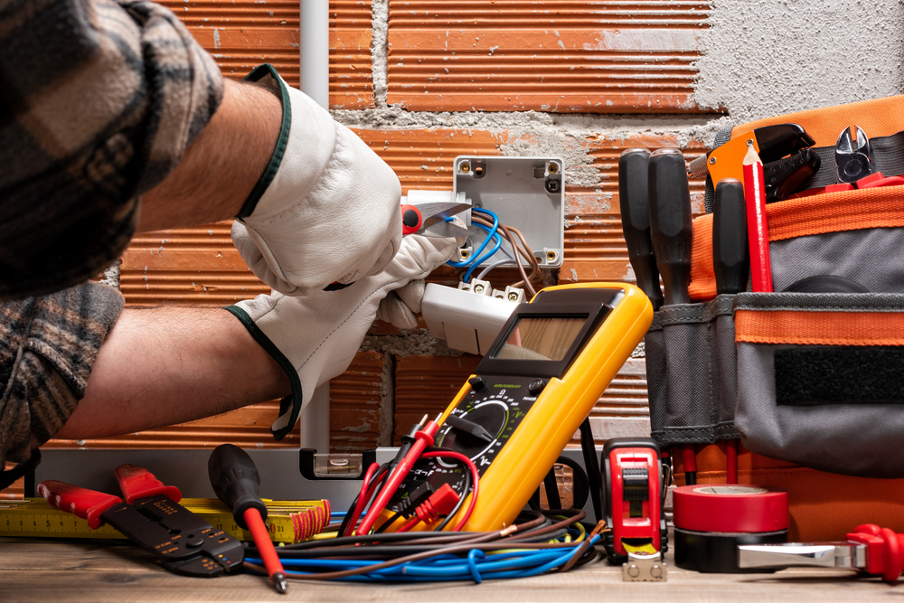 A person using tools to work on an electrical box with various electrical tools like digital multimeter,wire striper,tester etc.