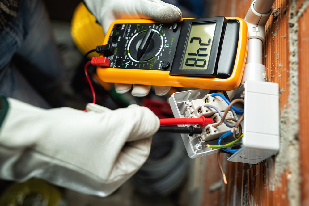 A person wearing gloves holds a multimeter, a device used to measure electrical properties.