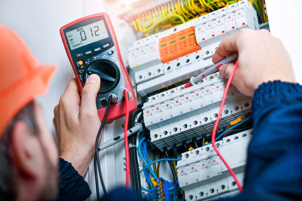 An electrical technician using a multimeter to inspect an electrical panel for potential issues.